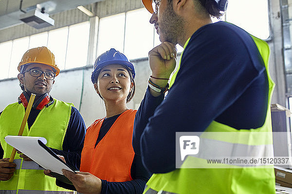 Two men and woman in reflective vests discussing in factory