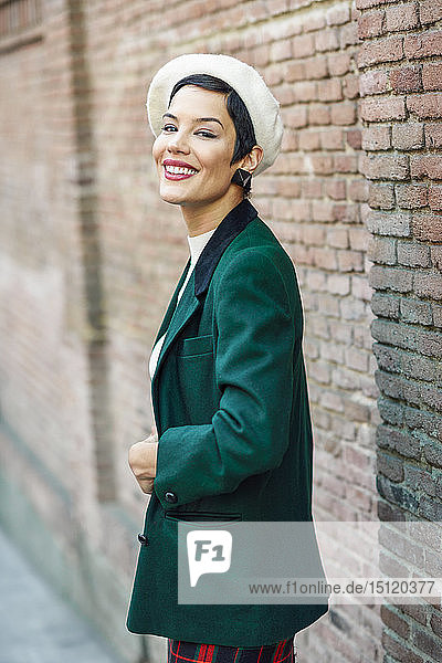 Portrait of smiling fashionable young woman at a brick wall
