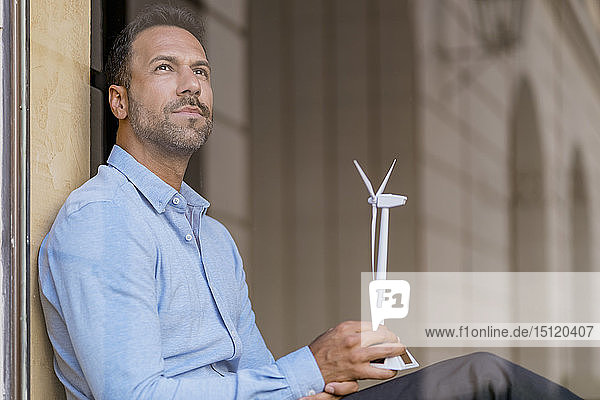 Geschäftsmann mit Windturbinenmodell hinter Fensterscheibendenken