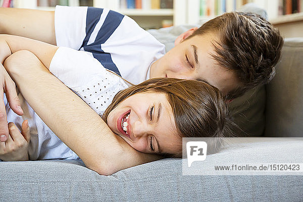 Porträt eines lachenden kleinen Mädchens  das zusammen mit seinem älteren Bruder auf der Couch liegt