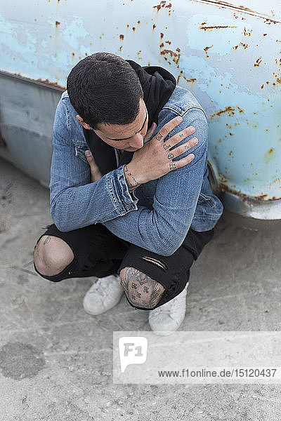Young amn crouching in front of a rusty car