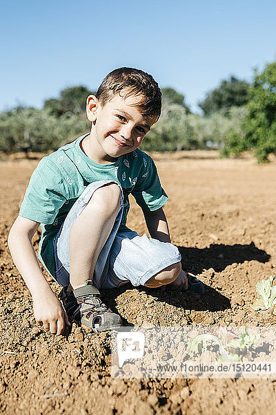 Spain  Tarragona. Boy looking at camera after planting lettuce in the garden