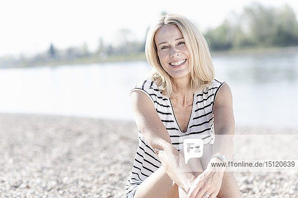 Porträt einer glücklichen  reifen Frau  die am Flussufer sitzt