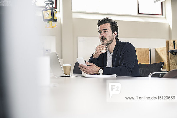Young businessman sitting in office  using laptop and smartphone
