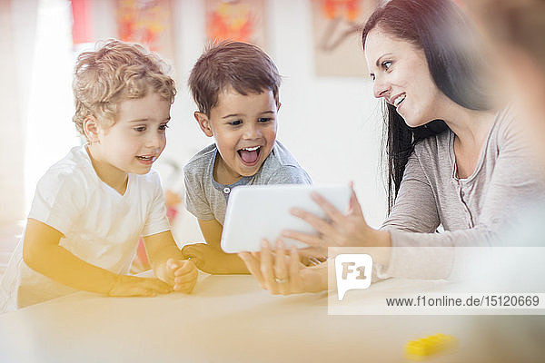 Vorschullehrerin zeigt glücklichen Jungen im Kindergarten eine Mini-Tablette