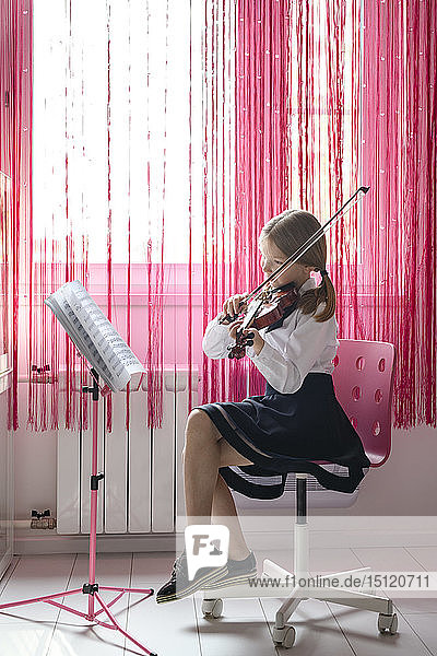 Mädchen  das zu Hause am Fenster sitzt und Geige spielt