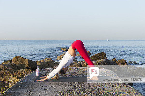 Junge Frau praktiziert Yoga am Strand und macht dabei einen nach unten gerichteten Hund