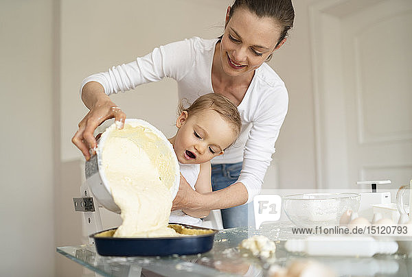 Mutter und kleine Tochter backen gemeinsam einen Kuchen und gießen Teig in die Backform