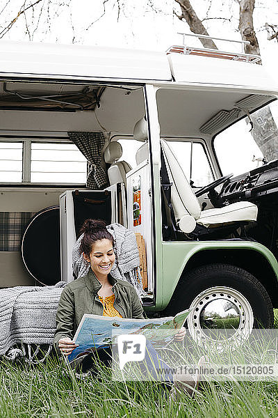 Young woman studying map  sitting in the grass  in front of her camper