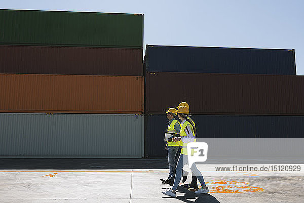Arbeiter gehen gemeinsam in der Nähe eines Stapels von Frachtcontainern auf einem Industriegelände