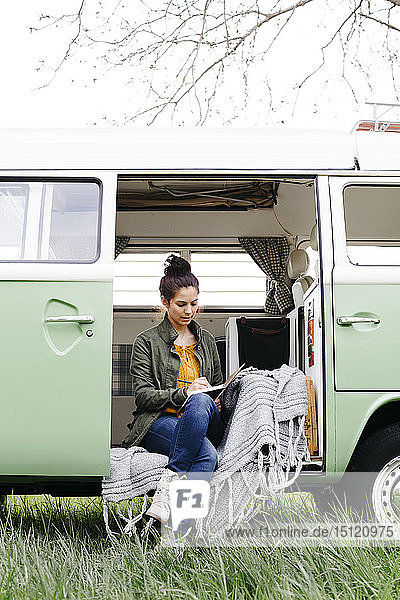 Young woman sitting in her camper  writing in a notebook