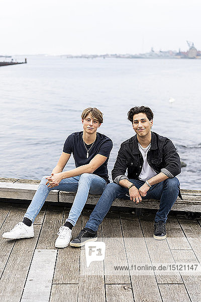 Dänemark  Kopenhagen  Porträt von zwei selbstbewussten jungen Männern  die am Wasser sitzen