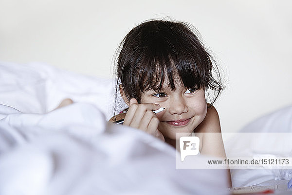 Porträt eines lächelnden kleinen Mädchens im Bett liegend mit Filzstift