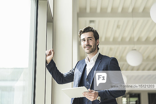 Erfolgreicher Manager steht in modernem Bürogebäude und benutzt Laptop