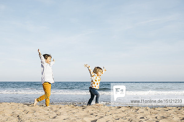 Glücklicher Junge und seine kleine Schwester laufen gemeinsam am Strand