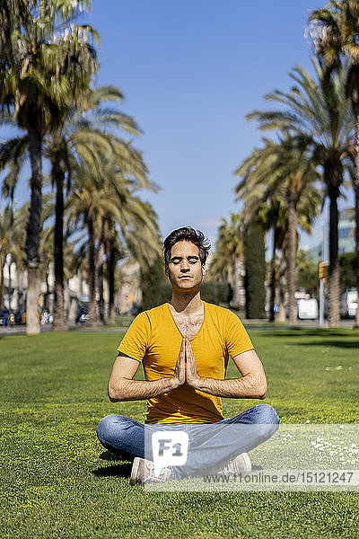 Spanien  Barcelona  Mann praktiziert Yoga auf dem Rasen in der Stadt