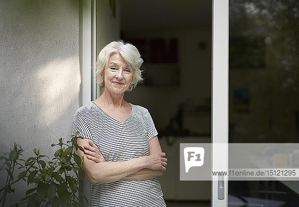 Portrait of smiling mature woman standing in front of open terrace door in the evening