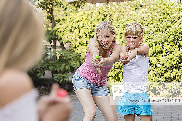 Mother and two girls splashing with water guns in garden