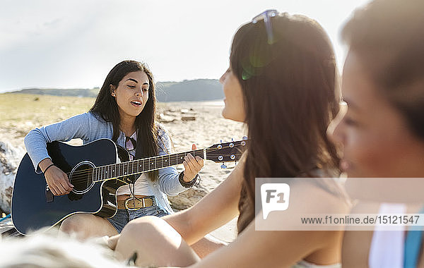 Junge Frau mit Freunden spielt Gitarre am Strand