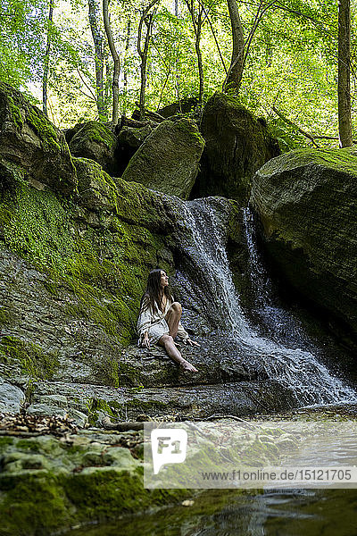 Junge Frau sitzt an einem Wasserfall  Garrotxa  Spanien