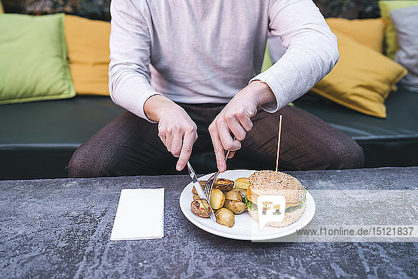 Young man sitting on couch in a restaurant having a vegan burger with potatoes for lunch