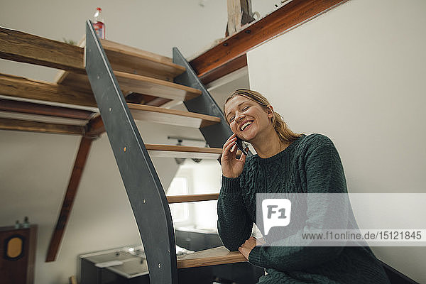 Glückliche junge Frau sitzt zu Hause auf der Treppe und telefoniert per Handy