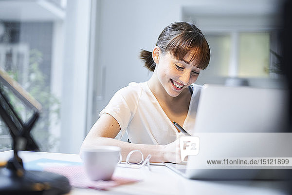 Lächelnde junge Frau arbeitet am Schreibtisch in einem Büro