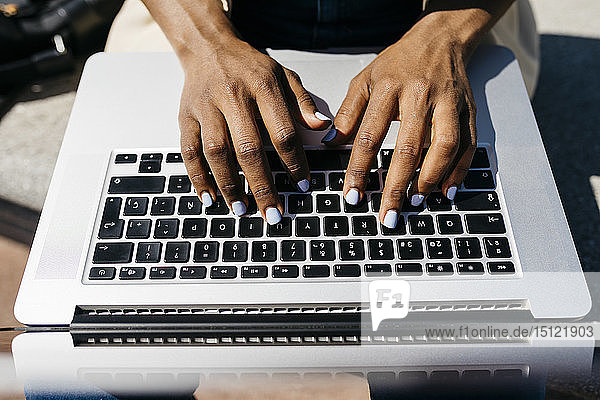 Geschäftsfrau  die auf einer Bank sitzt und am Laptop mit dem Finger tippt