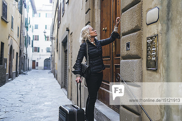 Italien  Florenz  reife Frau in Schwarz gekleidet  steht mit rollendem Koffer vor der Eingangstür