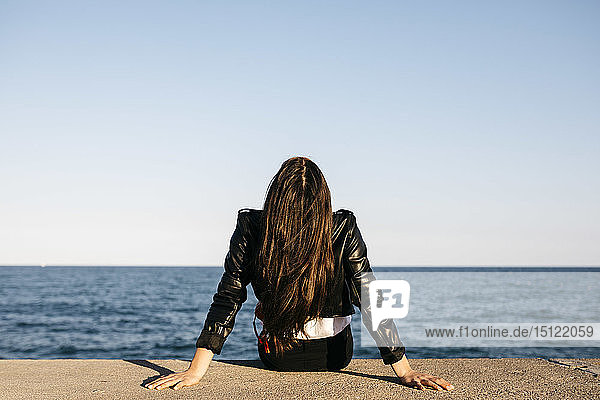 Junge Frau sitzt auf einer Mauer  im Hintergrund das Meer