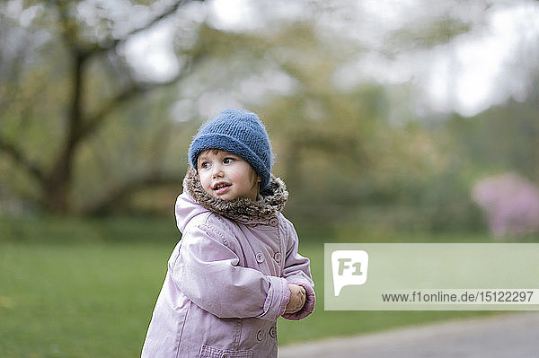 Bildnis eines kleinen Mädchens in einem Park mit blauem Hut und rosa Mantel
