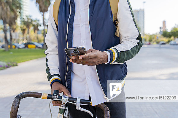 Close-up of casual businessman with bicycle using cell phone in the city  Barcelona  Spain