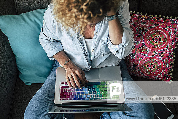 Frau benutzt Laptop mit mehrfarbiger Tastatur auf der Couch zu Hause