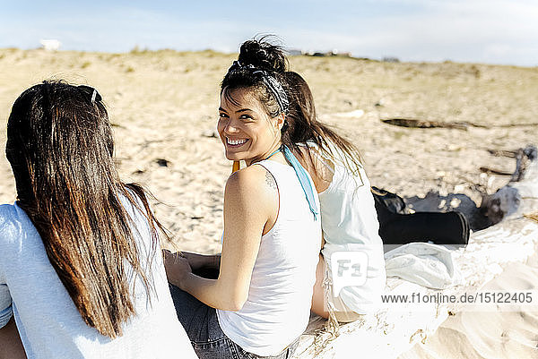 Glückliche Freundinnen sitzen auf einem Baumstamm am Strand