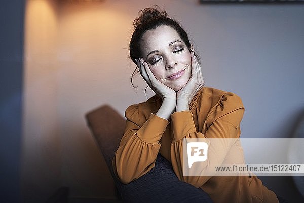 Porträt einer lächelnden Frau mit geschlossenen Augen  die zu Hause auf der Couch sitzt