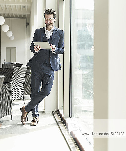 Young businessman standing in office building  using digital tablet  leaning on window