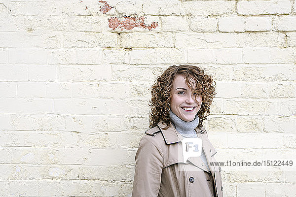 Porträt einer glücklichen Frau mit lockigem Haar vor einer Ziegelmauer