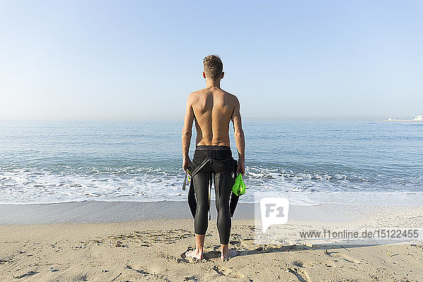 Rückansicht eines jungen Athleten am Strand  der sich auf das Schwimmen vorbereitet