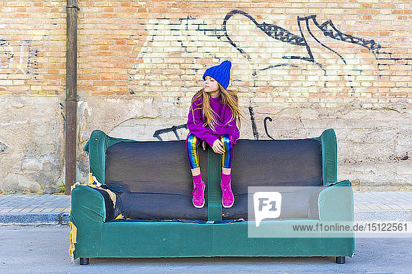 Girl wearing colorful clothing and sitting on a couch outdoors