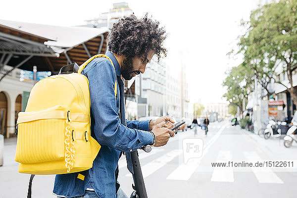 Mann mit Rucksack und E-Scooter mit Navigationsanwendung auf seinem Mobiltelefon in der Stadt  Barcelona  Spanien