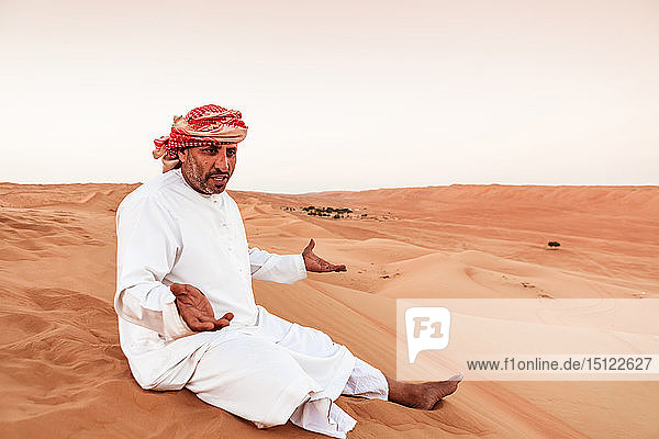 Beduine in Nationaltracht auf einer Sanddüne in der Wüste sitzend  Wahiba Sands  Oman