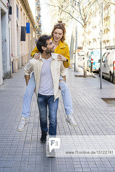 Man giving girlfriend a piggyback ride on pavement in the city