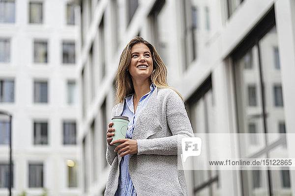 Junge Geschäftsfrau mit Kaffee zum Mitnehmen  im Hintergrund das Bürogebäude