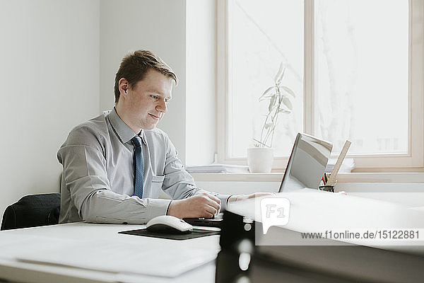 Young businessman using laptop at desk in office