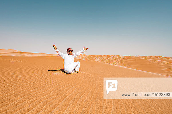 Beduine in Nationaltracht sitzen in der Wüste und heben die Arme  Wahiba Sands  Oman