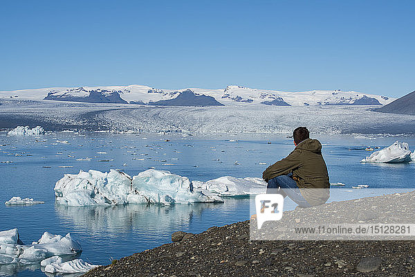 Junger Mann sitzt und bewundert die Aussicht auf die Gletscherlagune Jokulsarlon  Südostisland  Island  Polarregionen