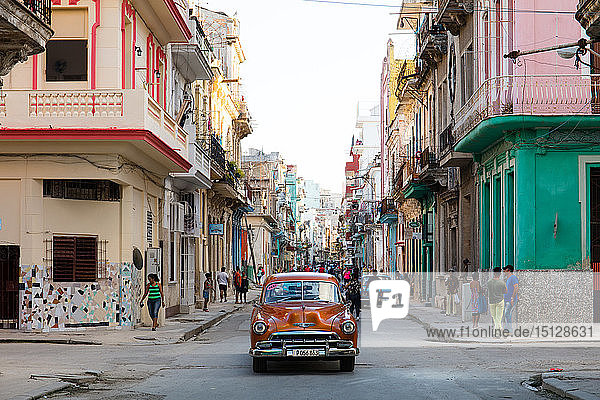 Roter Oldtimer fährt entlang alter bunter Straßen in Havanna  Kuba  Westindien  Karibik  Mittelamerika