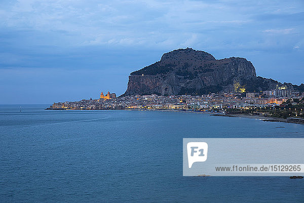 Blick entlang der Küste auf die Stadt und die beleuchtete Kathedrale  Abenddämmerung  La Rocca überragend  Cefalu  Palermo  Sizilien  Italien  Mittelmeer  Europa