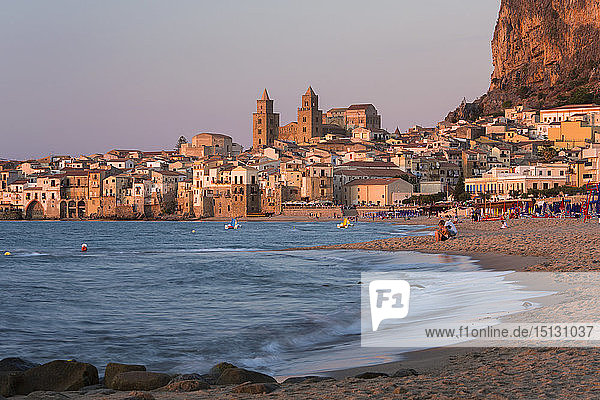 Blick vom Strand entlang der Wasserkante auf die Stadt und die zum UNESCO-Weltkulturerbe gehörende arabisch-normannische Kathedrale  Sonnenuntergang  Cefalu  Palermo  Sizilien  Italien  Mittelmeer  Europa