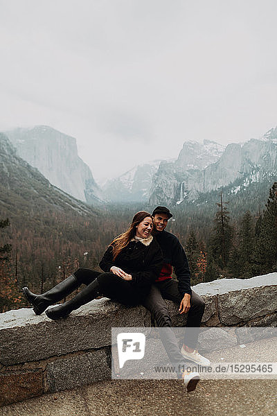 Happy young couple sitting on wall in mountain landscape  Yosemite Village  California  USA